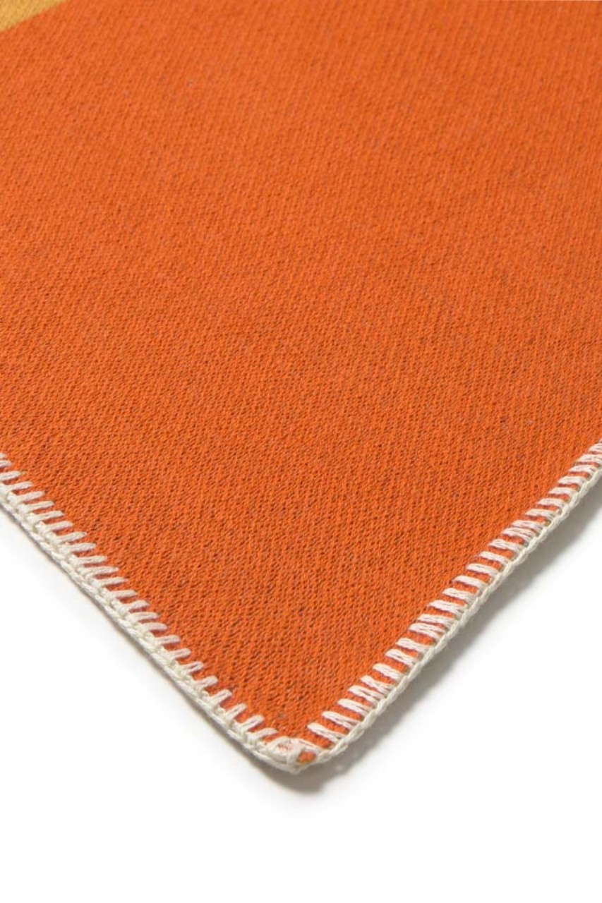 Nahaufnahme einer strukturierten Decke aus orangefarbenem Stoff mit einem dekorativen weißen Überwendlingsstich-Rand auf weißem Hintergrund.